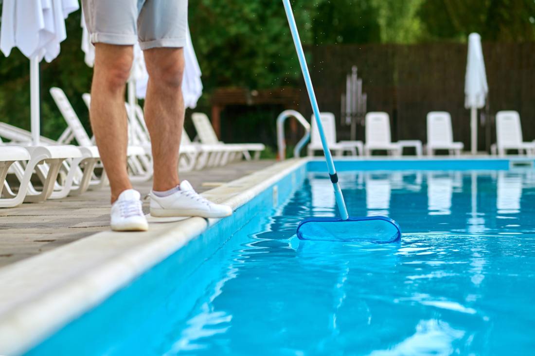 A technician skimming a resort pool lined with lounge chairs