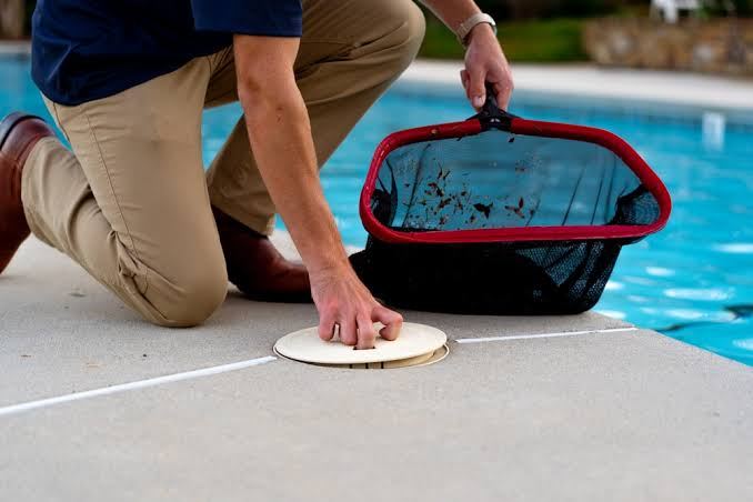 A technician checking a skimmer basket at a backyard pool